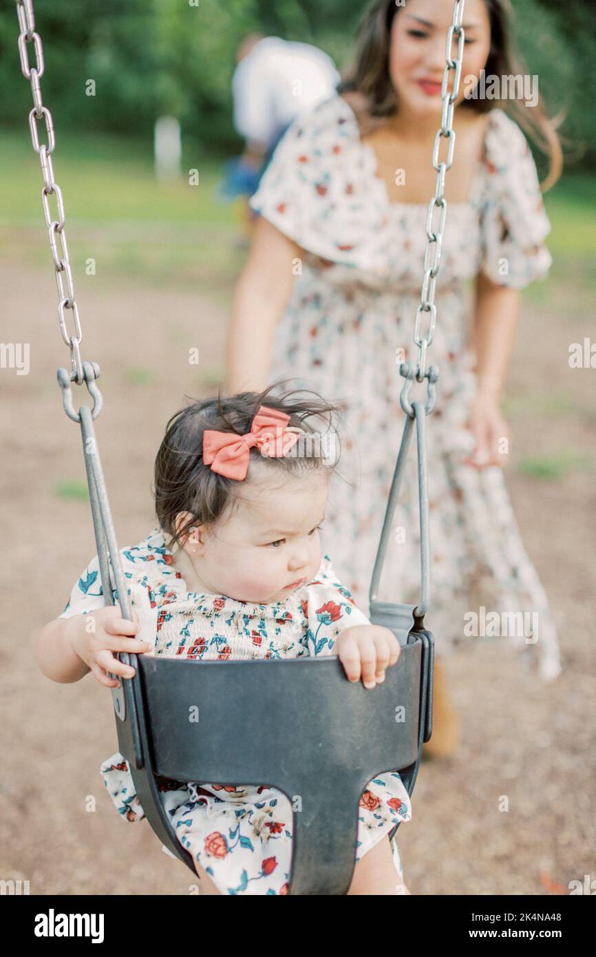 1-year old multiracial girl is pushed on a swing by her Asian mother ...
