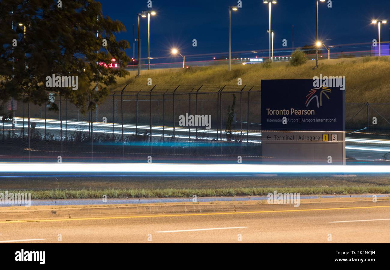 A directional sign for the Toronto Pearson Intl. Airport terminals, seen at night with vehicle light trails surrounding the area. Stock Photo