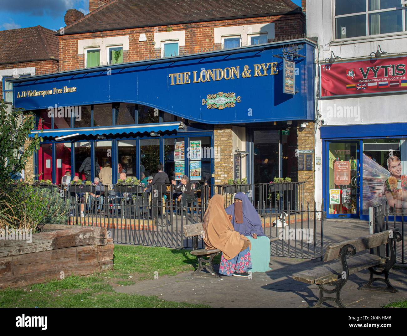 London, UK. Sept 29 2022 . Muslim woman sitting next to Weatherspoon Free House , The London & Rey pub . Stock Photo
