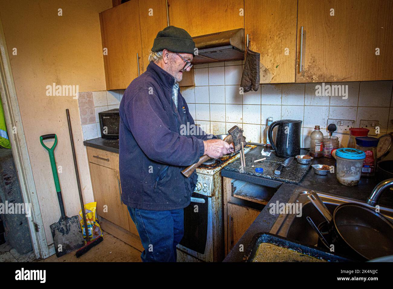 London, UK. Sept 29 2022 .Man chops firewood with an axe in his kitchen Stock Photo