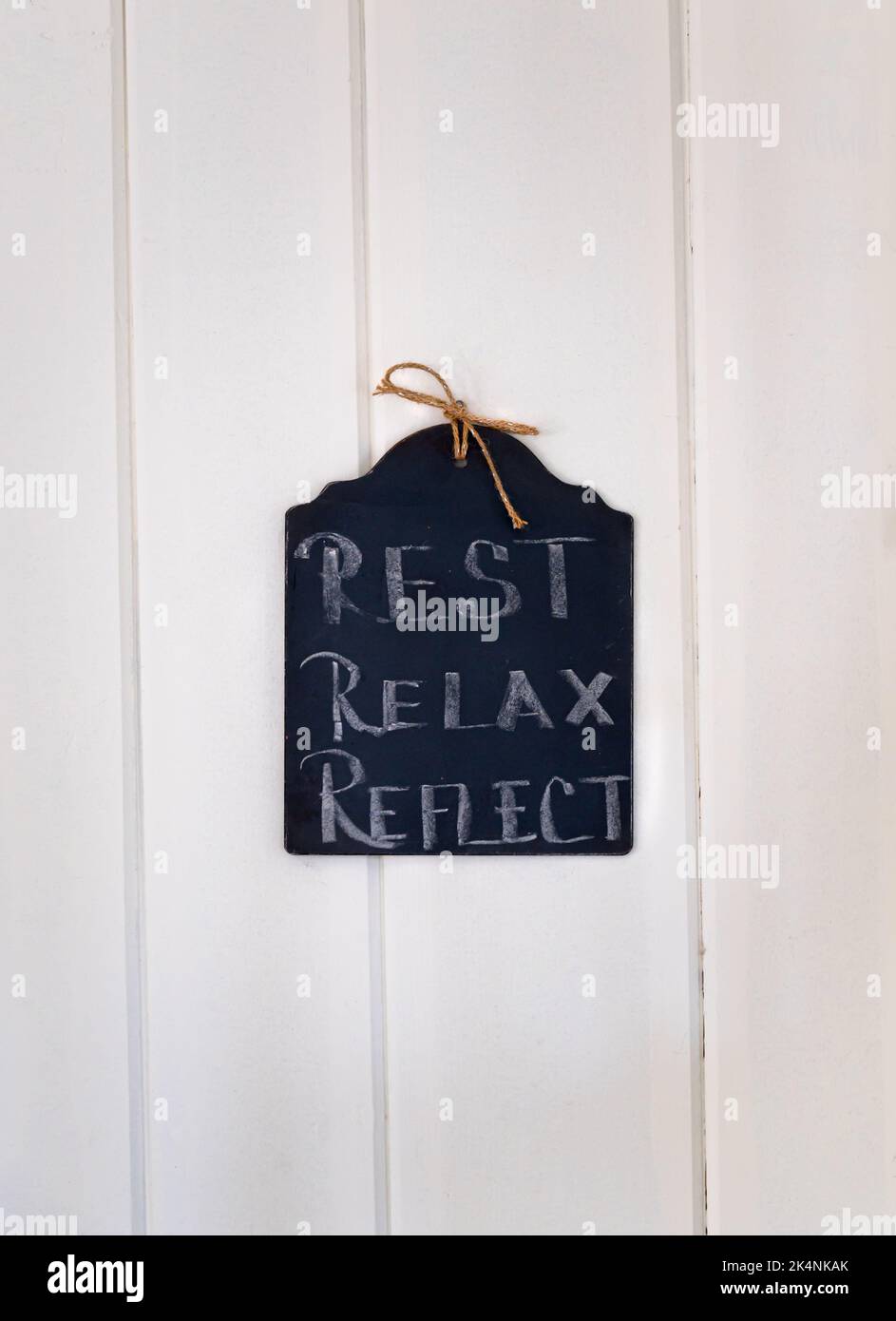 Black chalkboard sign that reads 'Rest, Relax, Reflect' on a white shiplap wall Stock Photo