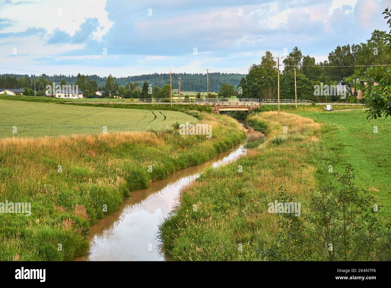 A small river flowing through green fields under a blue cloudy sky ...