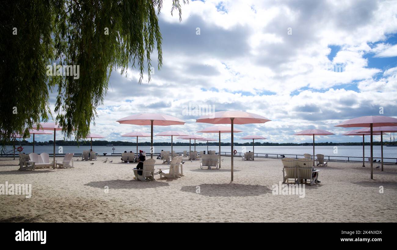 A public beach park with pink umbrellas and Muskoka chairs Stock Photo