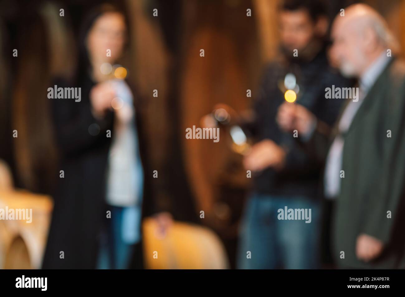 Blurred wine cellar guests, one woman and two men tasting a white wine produced and aged by an old traditions in oak barrels Stock Photo