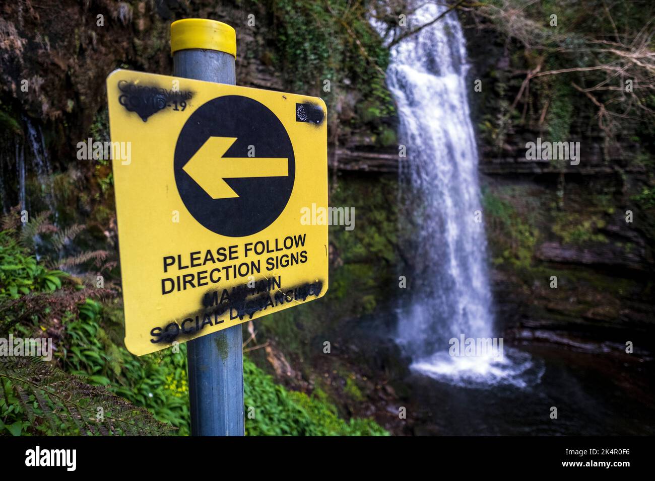 Vandalized sign asking hikers to social distance, Glencar Waterfall, County Leitrim, Ireland Stock Photo