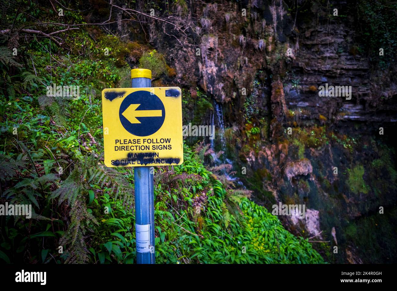 Vandalized sign asking hikers to social distance, Glencar Waterfall, County Leitrim, Ireland Stock Photo