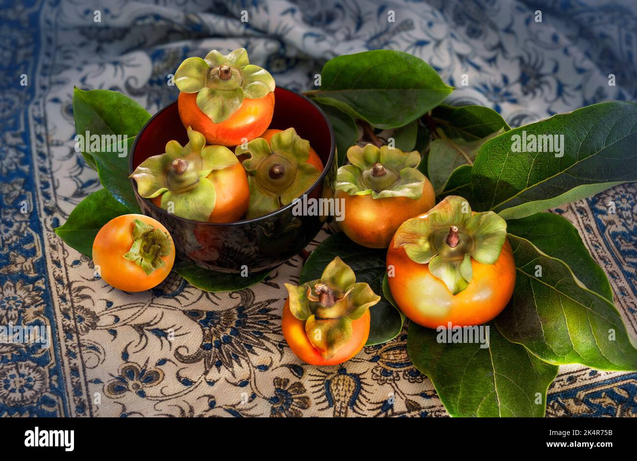 fresh ripe persimmons on patterned fabric cloth background Stock Photo