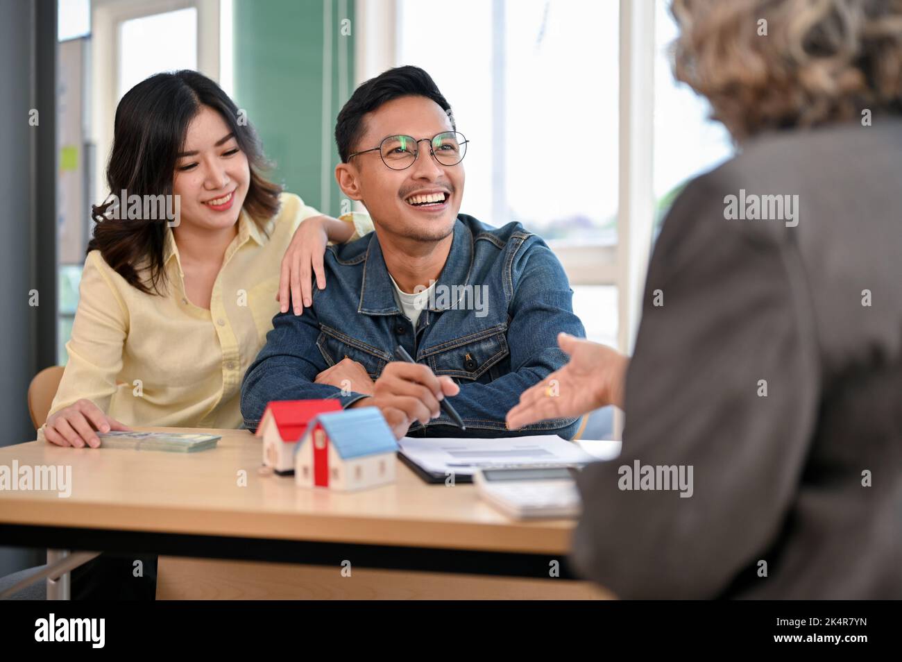 Lovely Asian couple meets with their real estate agent or apartment realtor to discuss and summarize the householder's insurance and down payment. Stock Photo