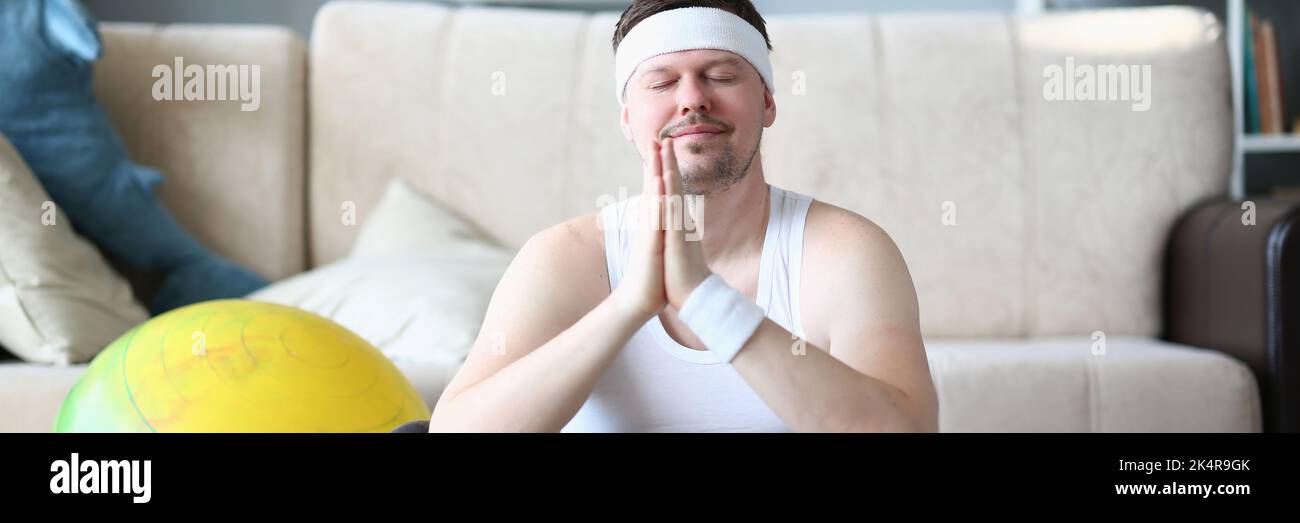 Man with praying hands and closed eyes meditates in lotus position at home Stock Photo