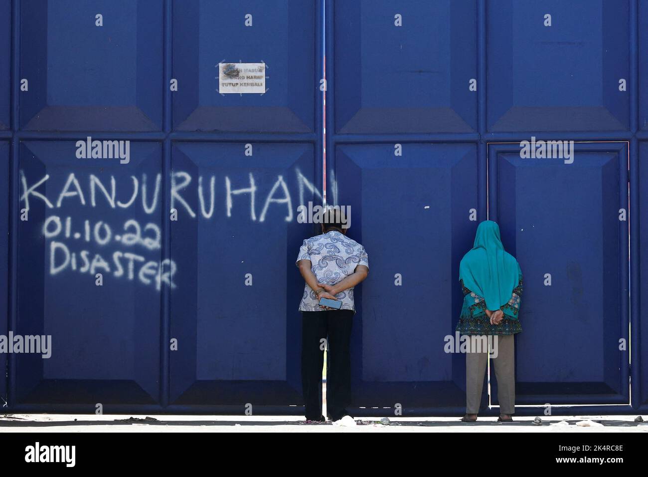 People peek through a gate, following a riot and stampede after a