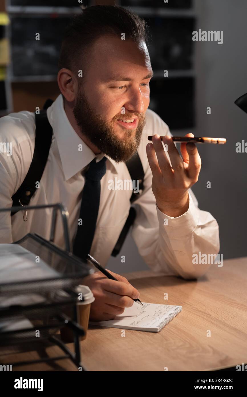 Portrait of a police officer or investigator working in the office at the table dictating information on the phone, smartphone voice assistant Stock Photo