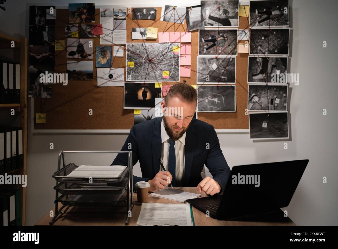 detective man working with evidence at desk in office, evidence board in the background Stock Photo