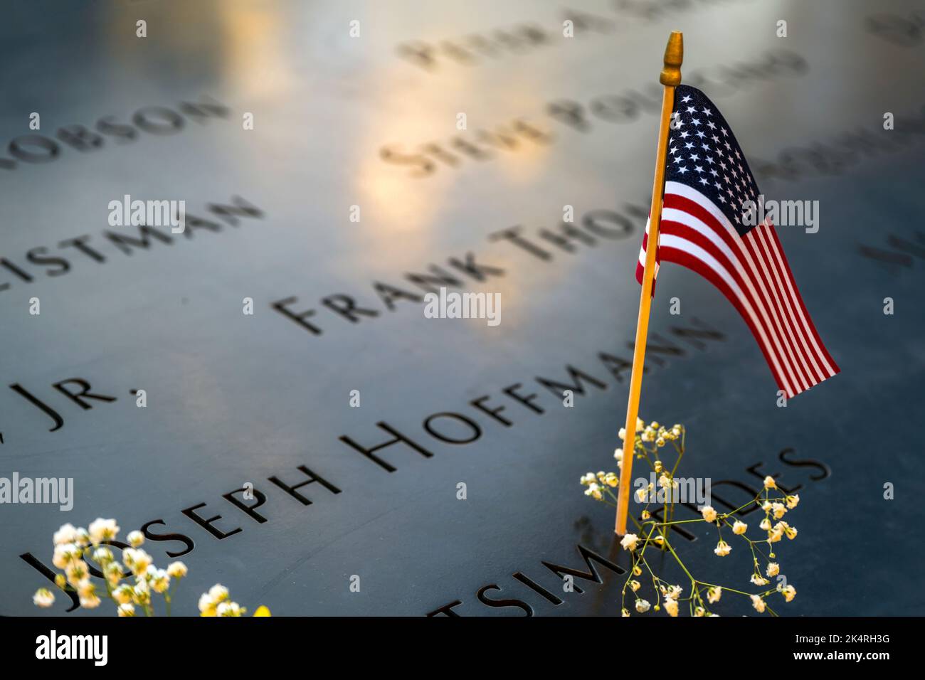 US flag and flowers on the parapet boarding the pool of the National September 11 Memorial & Museum, Manhattan, New York, USA Stock Photo