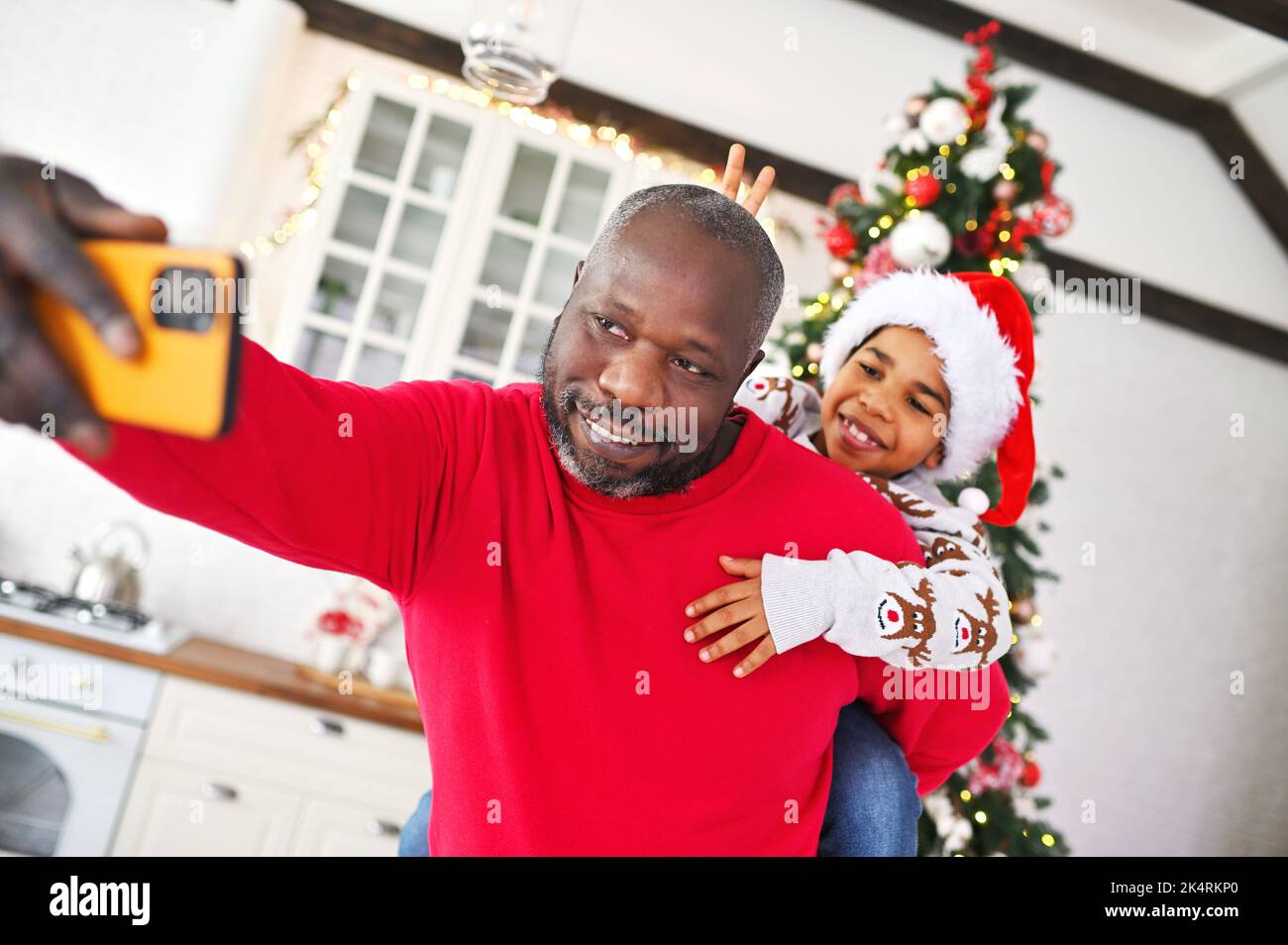 Father With A Little Son On His Shoulders In A Santa Hat Smiling While