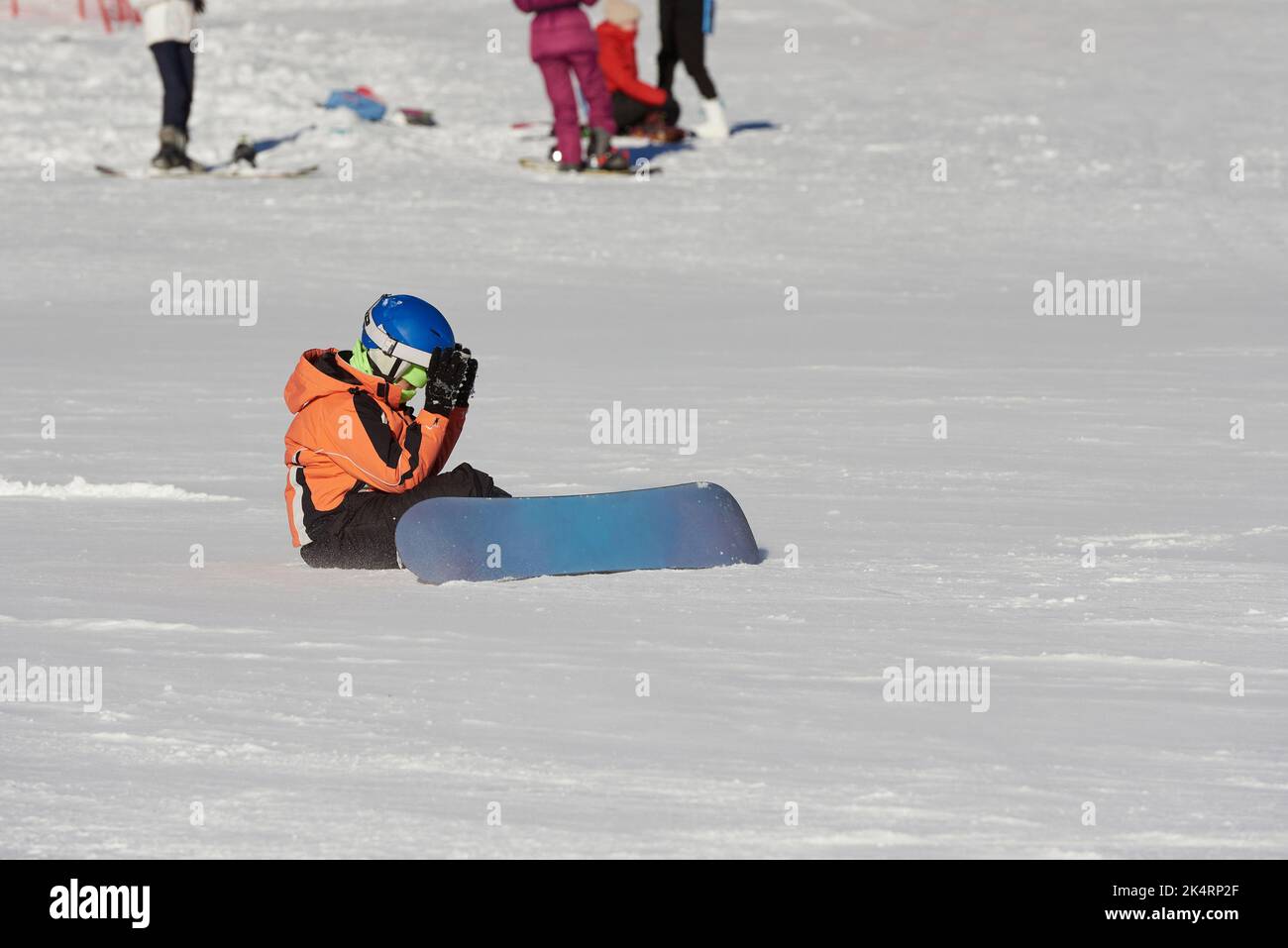 Young snowboarder failed on the ski slope and sits on the snow. Stock Photo