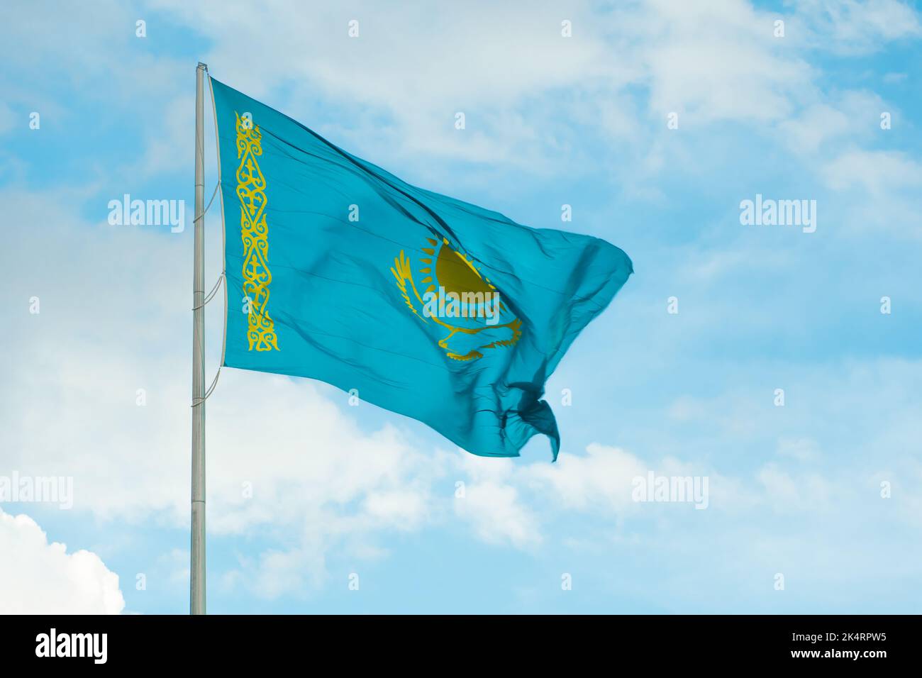 Flag of Kazakhstan on sky background. Waving flag of Republic of Kazakhstan. Fabric textures flowing flag of Kazakhstan. Stock Photo