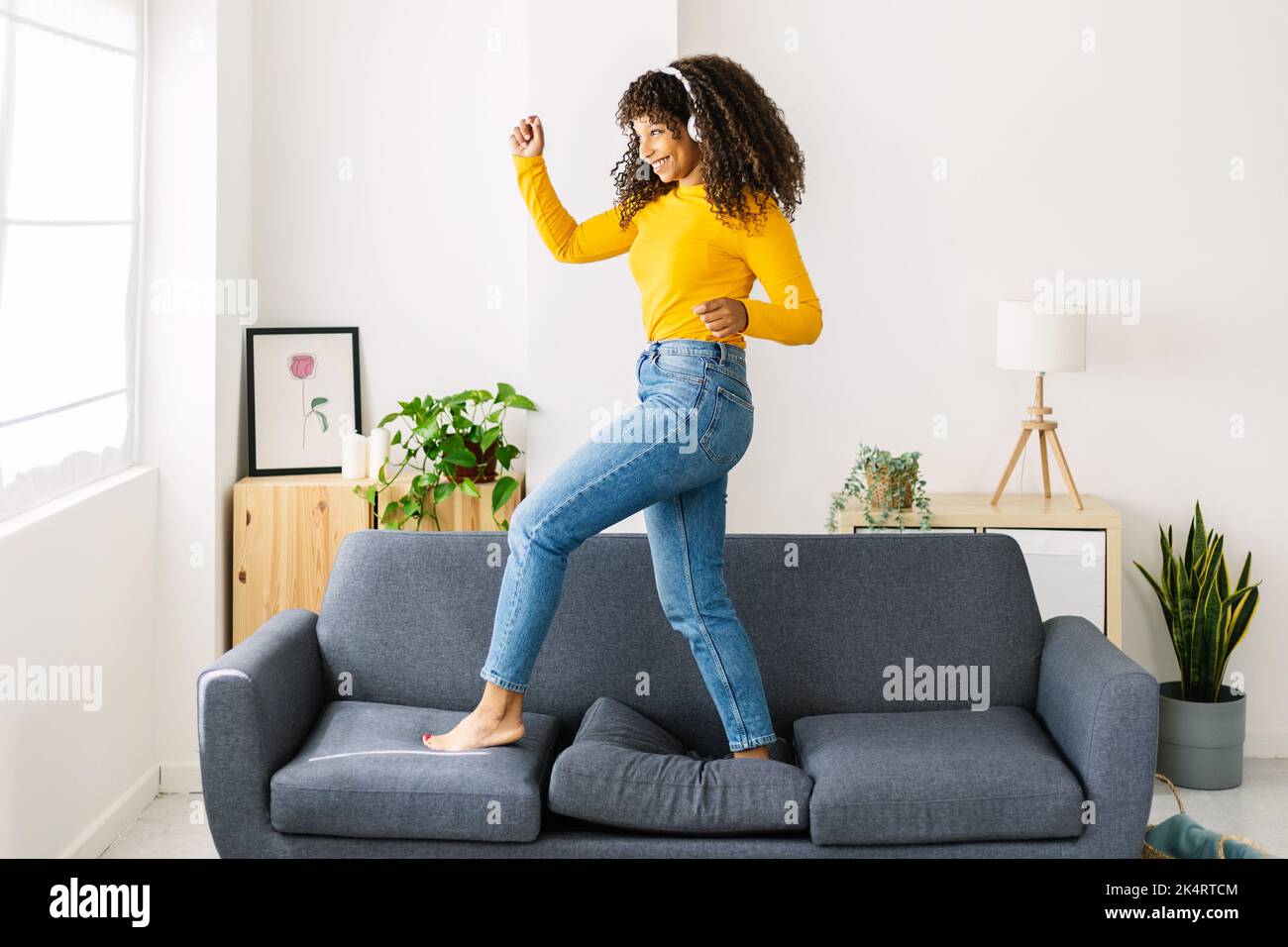 Excited african american woman dancing on sofa while listening to music Stock Photo
