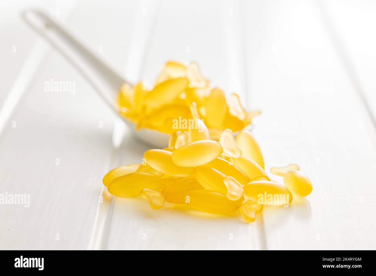 Fish oil capsules. Yellow omega 3 pills in spoon on the white table. Stock Photo