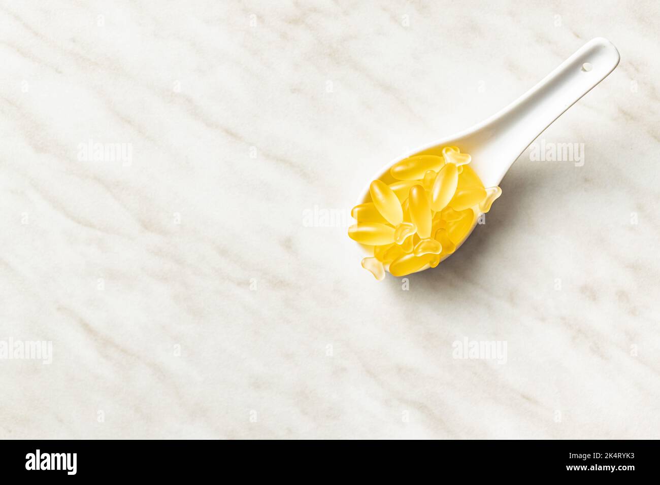 Fish oil capsules. Yellow omega 3 pills in spoon on the white table. Top view. Stock Photo