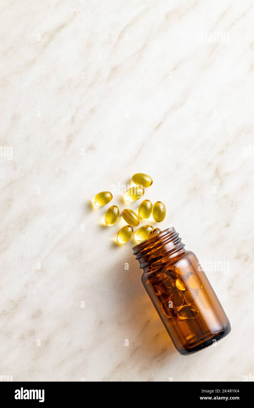 Fish oil capsules. Yellow omega 3 pills in glass bottle on the white table. Top view. Stock Photo