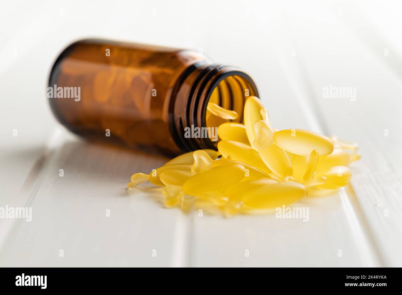 Fish oil capsules. Yellow omega 3 pills in glass bottle on the white table. Stock Photo