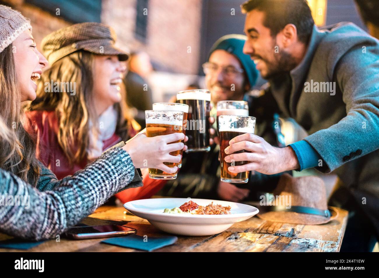 Friendly guys approaching happy girls at brewery pub outdoor on winter time - Friendship concept with young people having drunk fun together drinking Stock Photo