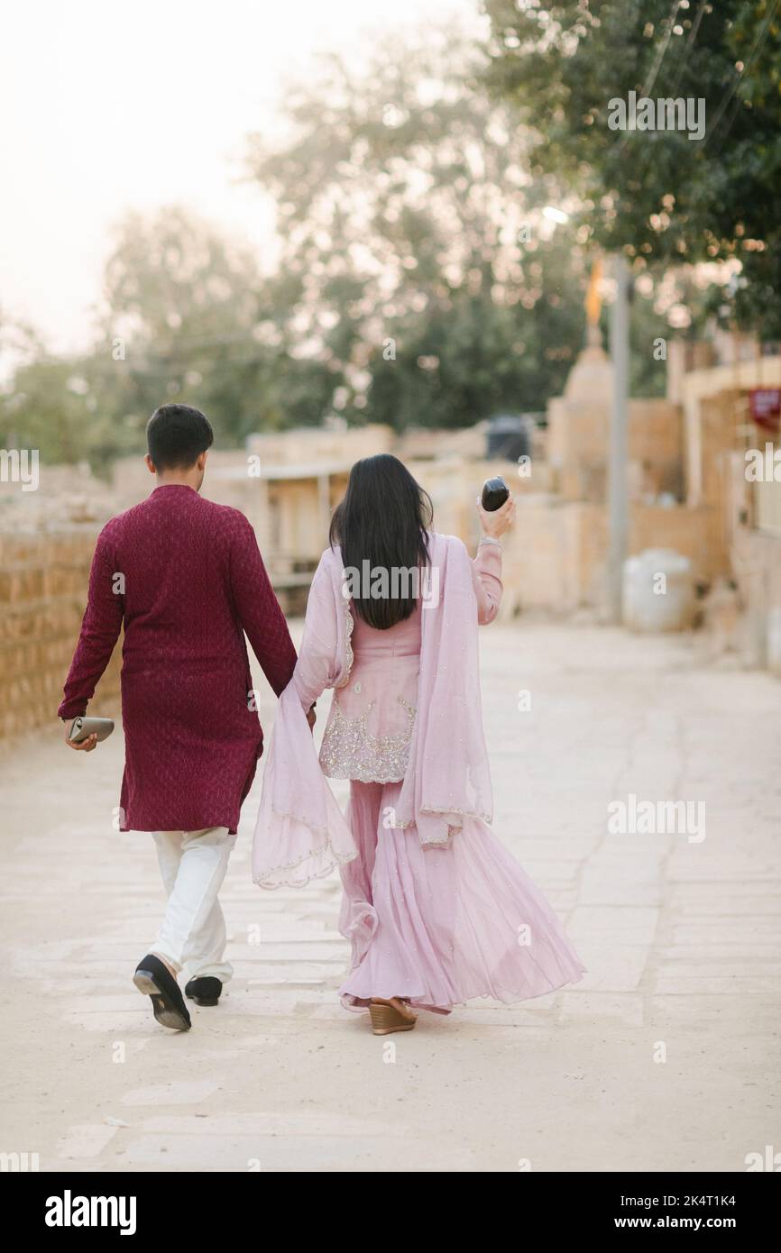 A vertical shot of a young Indian couple walking down the street ...