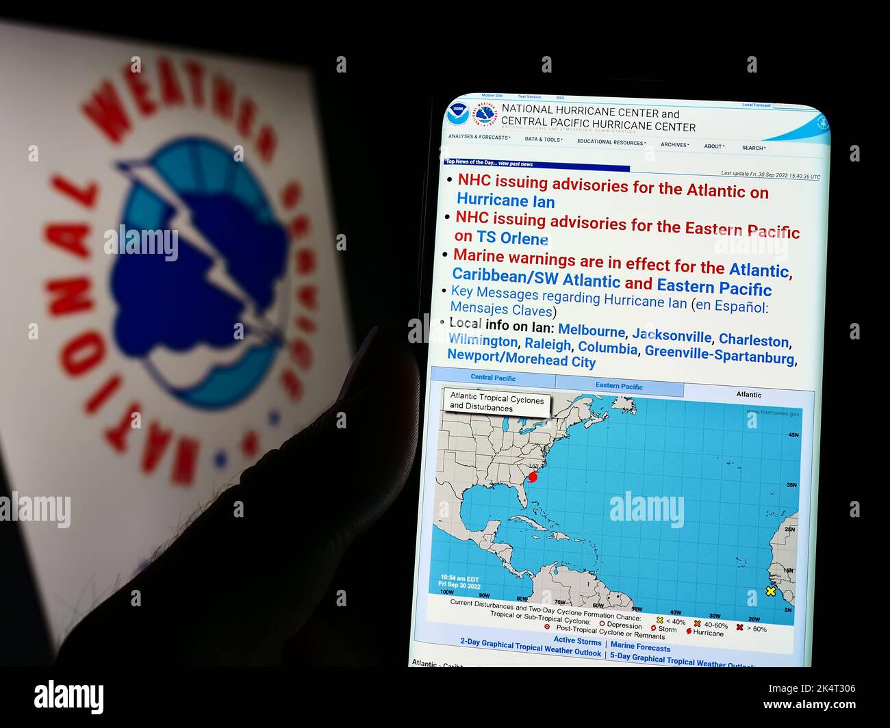 Person holding smartphone with website of US NWS division National Hurricane Center (NHC) on screen with logo. Focus on center of phone display. Stock Photo