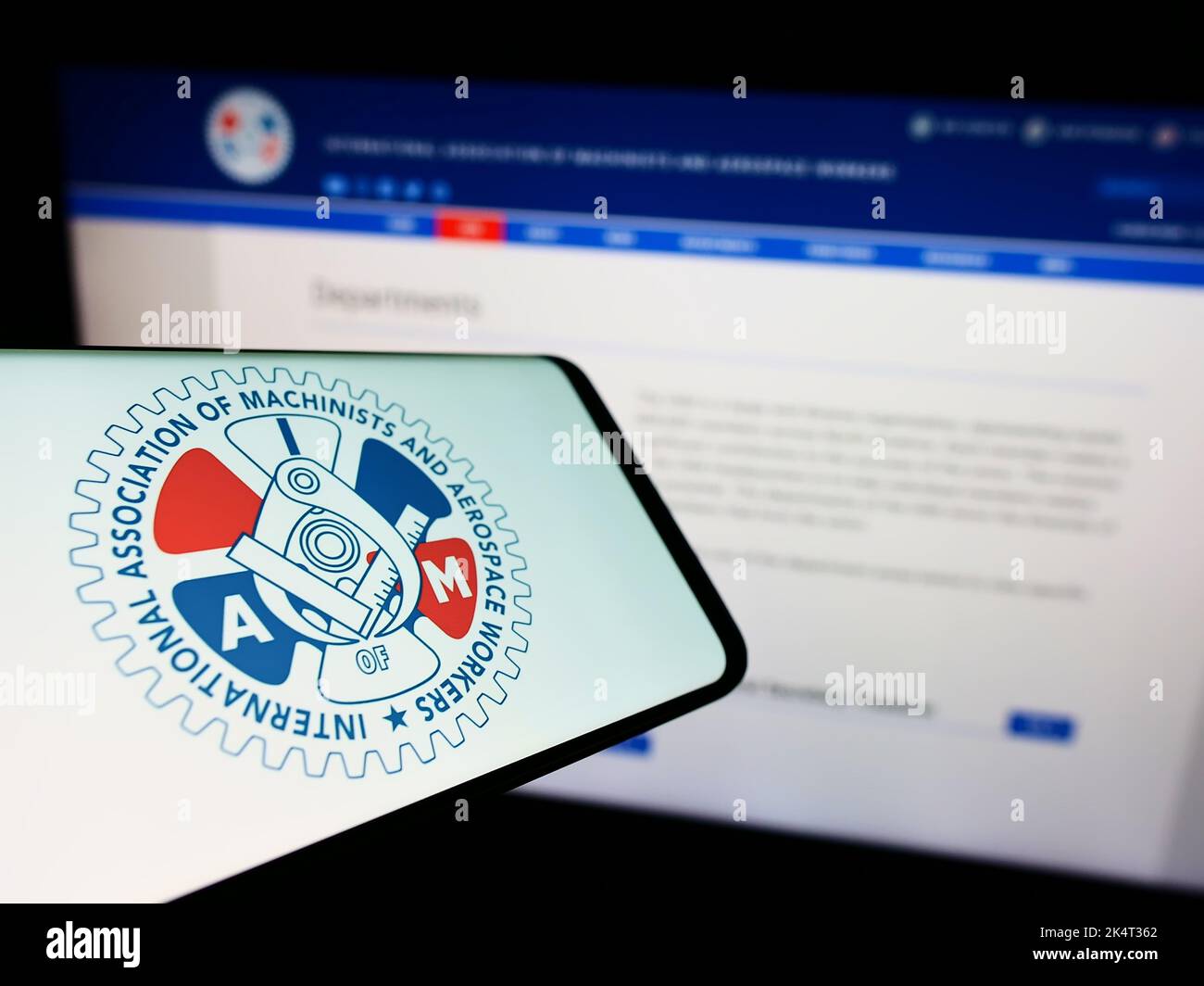 Mobile phone with logo of American-Canadian trade union IAM on screen in front of website. Focus on center-right of phone display. Stock Photo