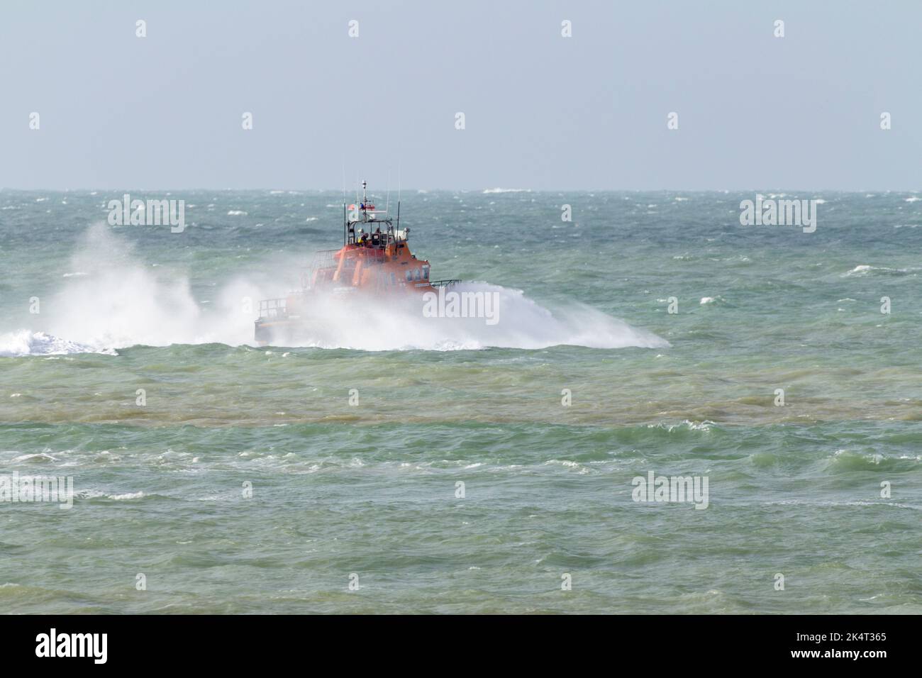 Newhaven lifeboat orange and blue going out to sea with high winds and sea spray around the vessel strong waves also rocking the boat Stock Photo