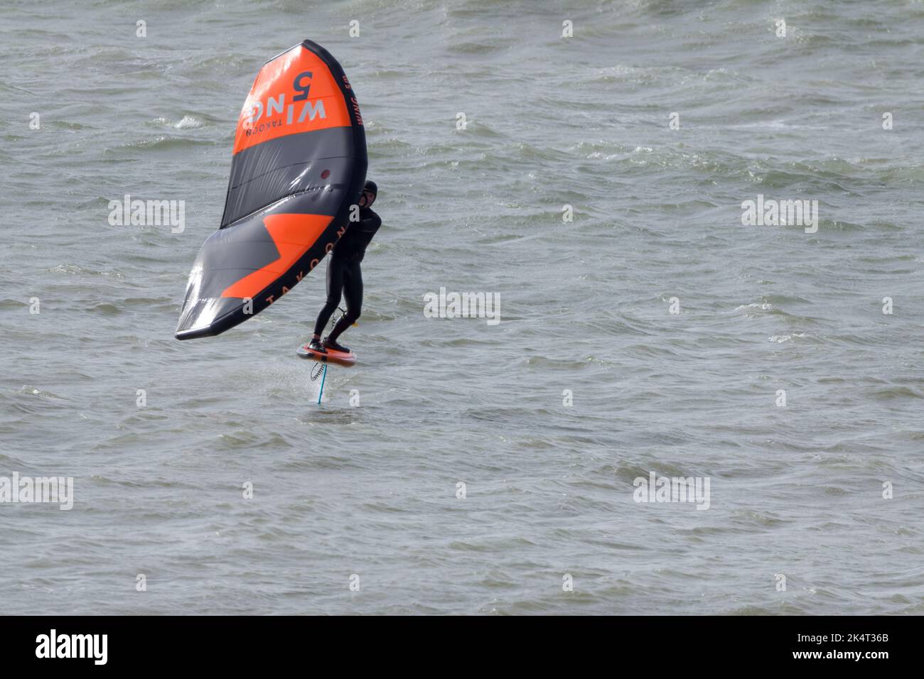 Water sport surfing in the sea with sails for catching the wind to propel the board and surfer. A hydrofoil under the board lifts board above water. Stock Photo