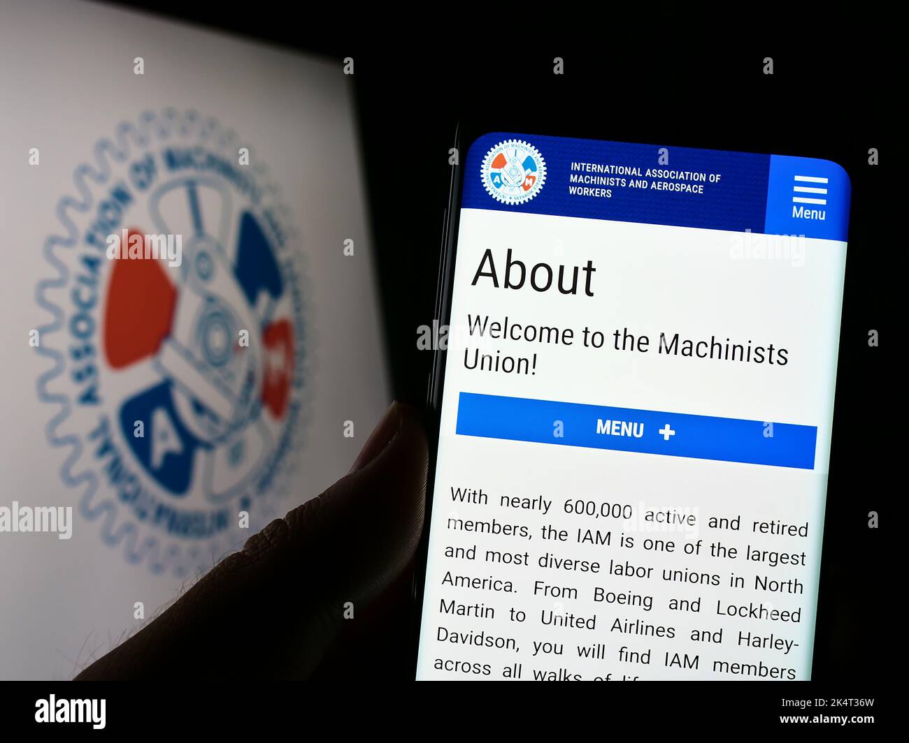 Person holding cellphone with webpage of American-Canadian trade union IAM on screen in front of logo. Focus on center of phone display. Stock Photo