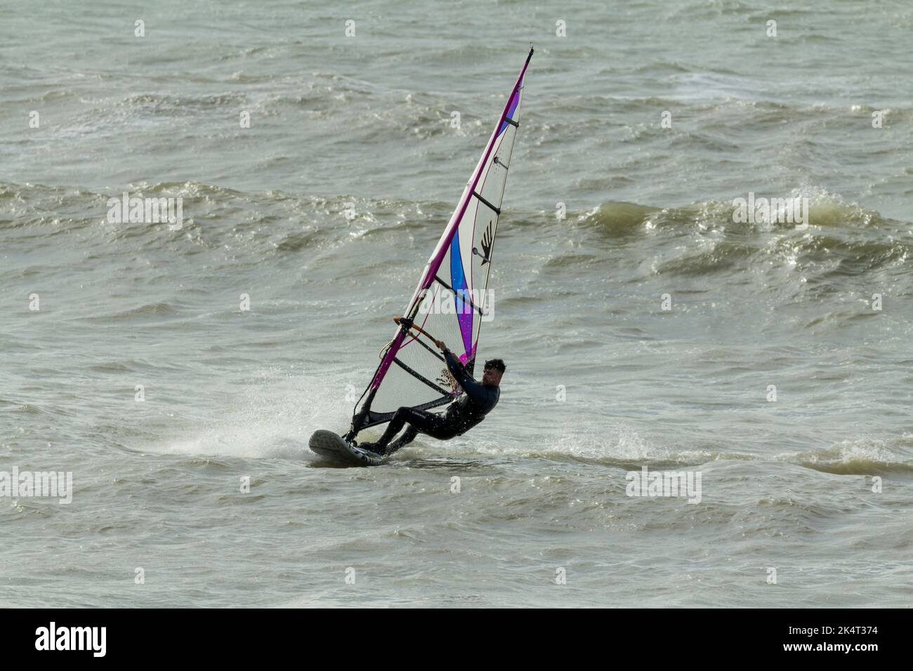 Water sport wind surfing in the sea with sail for catching the wind to propel the board and surfer sail is tilted and turned to steer and catch wind Stock Photo