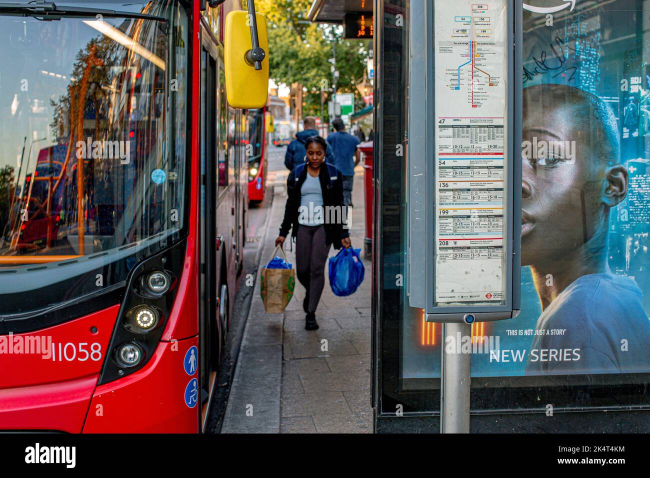 London, UK. Sept 29 2022 .A red double-decker bus  and woman with shopping bags at bus stop in Lewisham. Stock Photo