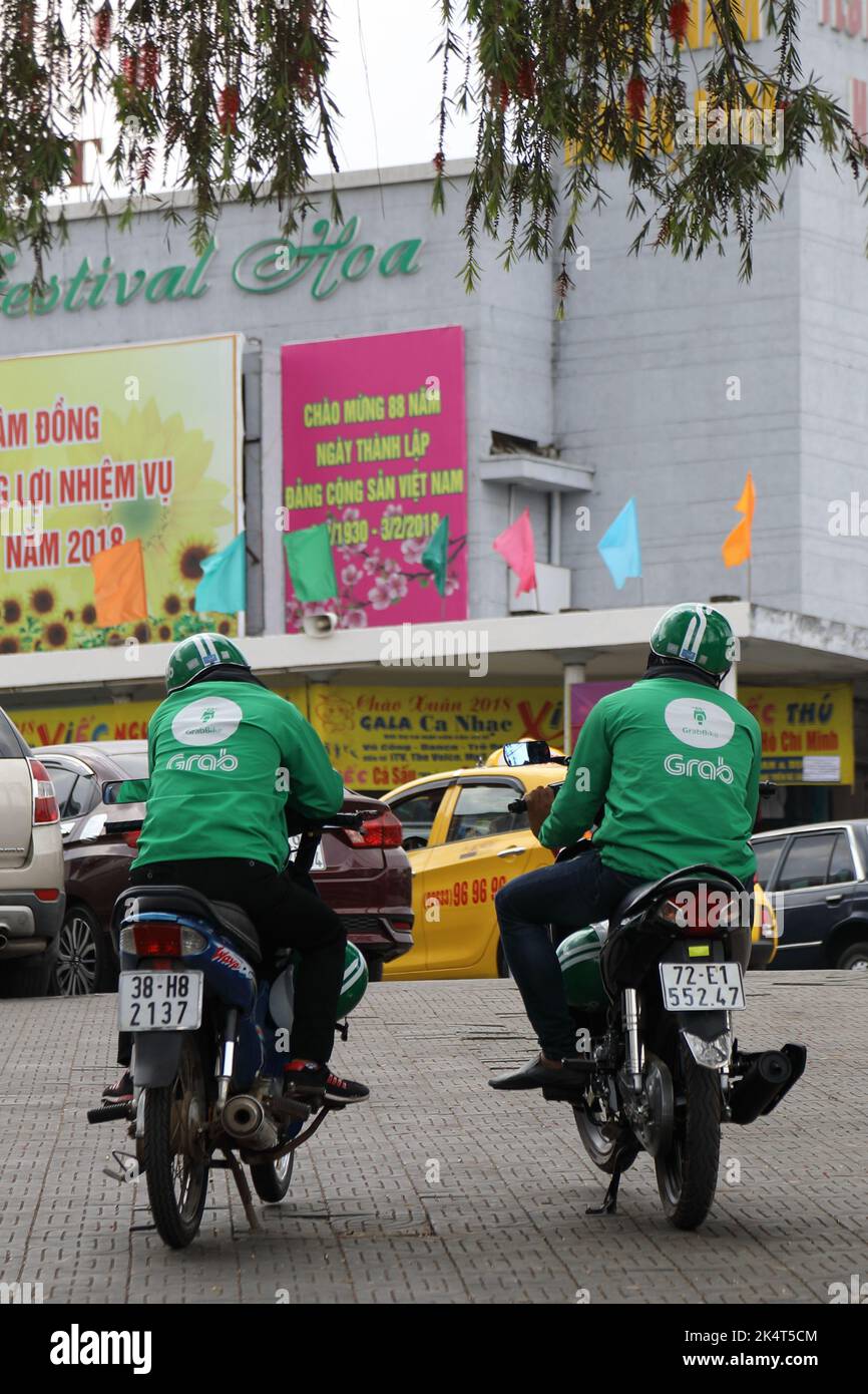 Two Grab motorcyclists are waiting opposite Hoa Binh Theatre for order in  the mid-day under wilow tree shadow Stock Photo