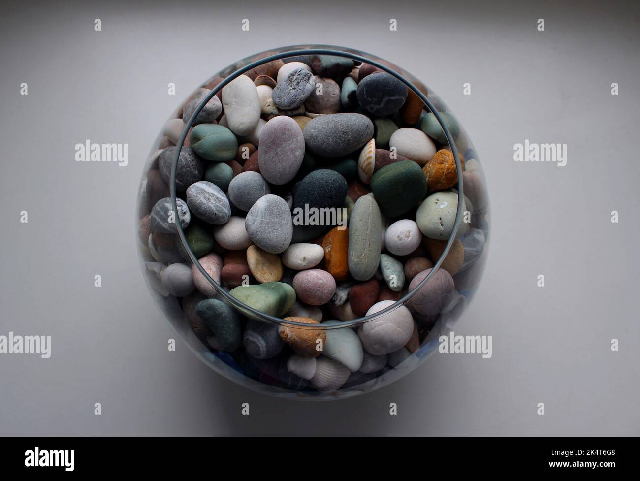 Round glass vase with colorful smooth pebbles and shells on a white