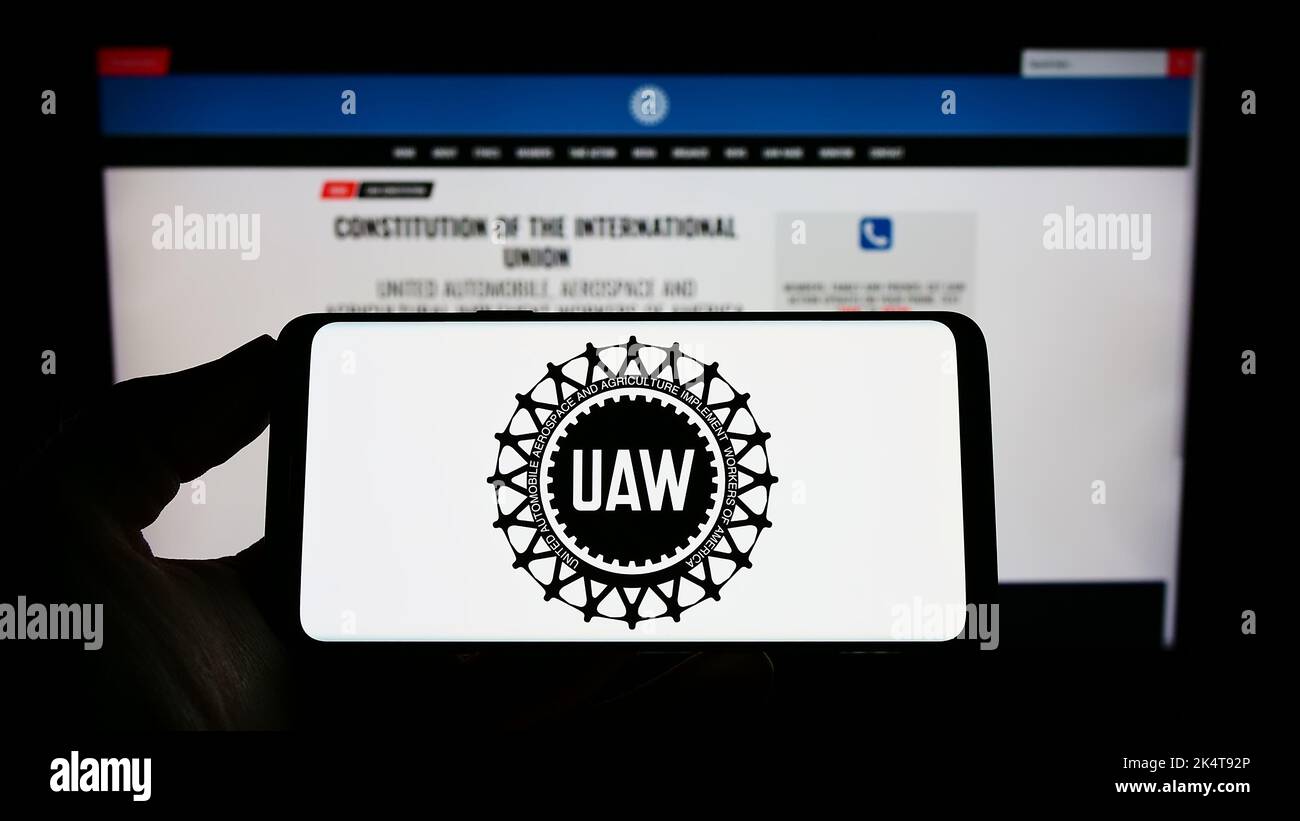 Person holding cellphone with logo of American trade union United Auto Workers (UAW) on screen in front of webpage. Focus on phone display. Stock Photo