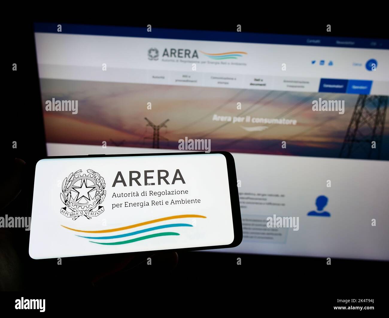 Person holding smartphone with logo of Italian regulation authority ARERA on screen in front of website. Focus on phone display. Stock Photo