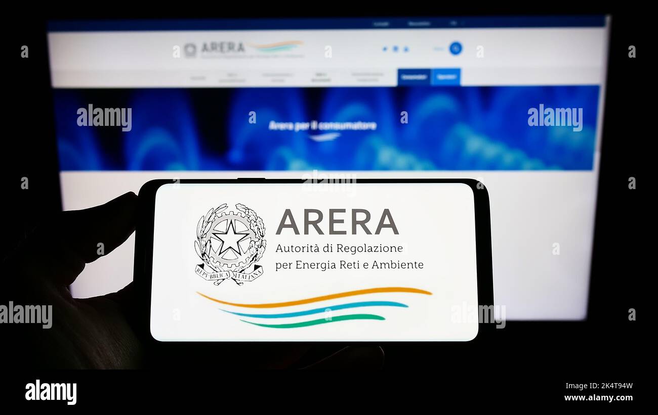 Person holding mobile phone with logo of Italian regulation authority ARERA on screen in front of web page. Focus on phone display. Stock Photo