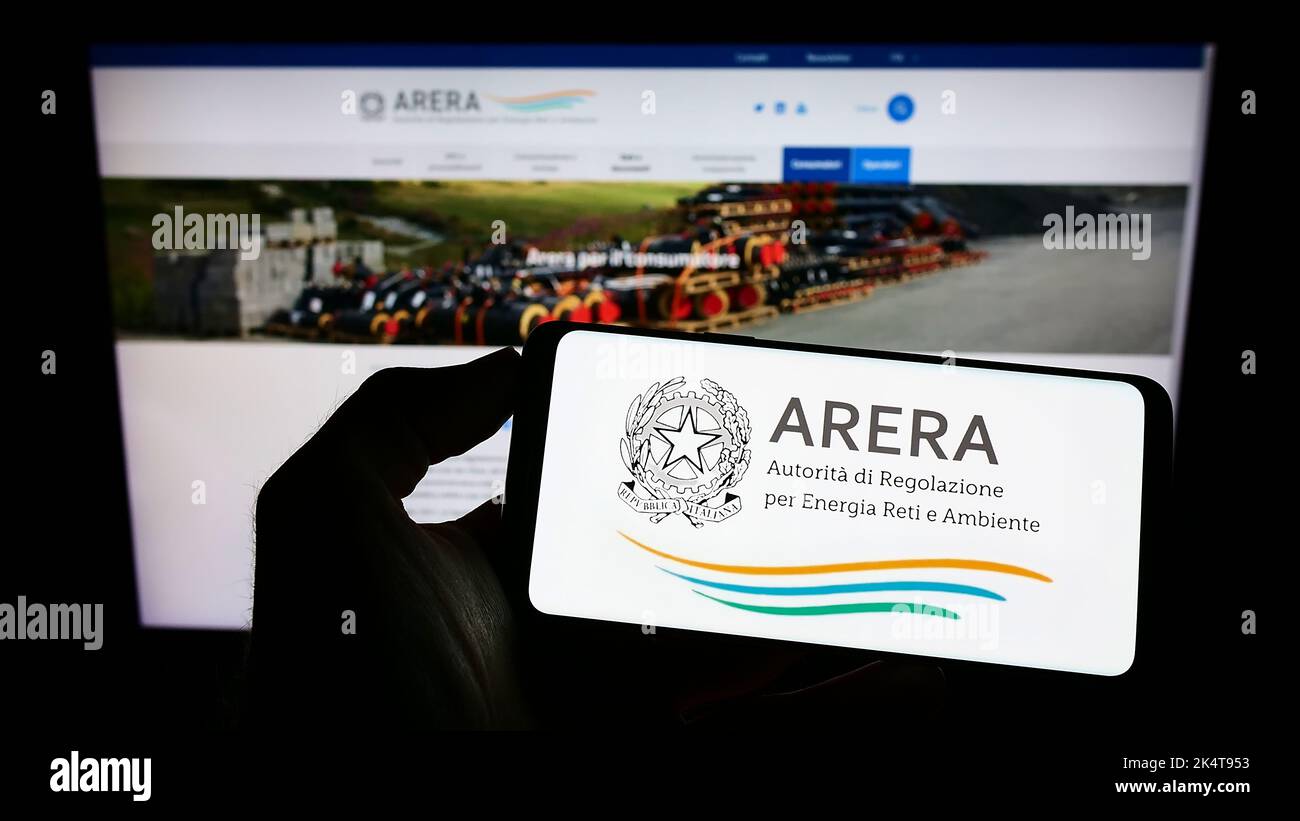 Person holding cellphone with logo of Italian regulation authority ARERA on screen in front of wepage. Focus on phone display. Stock Photo