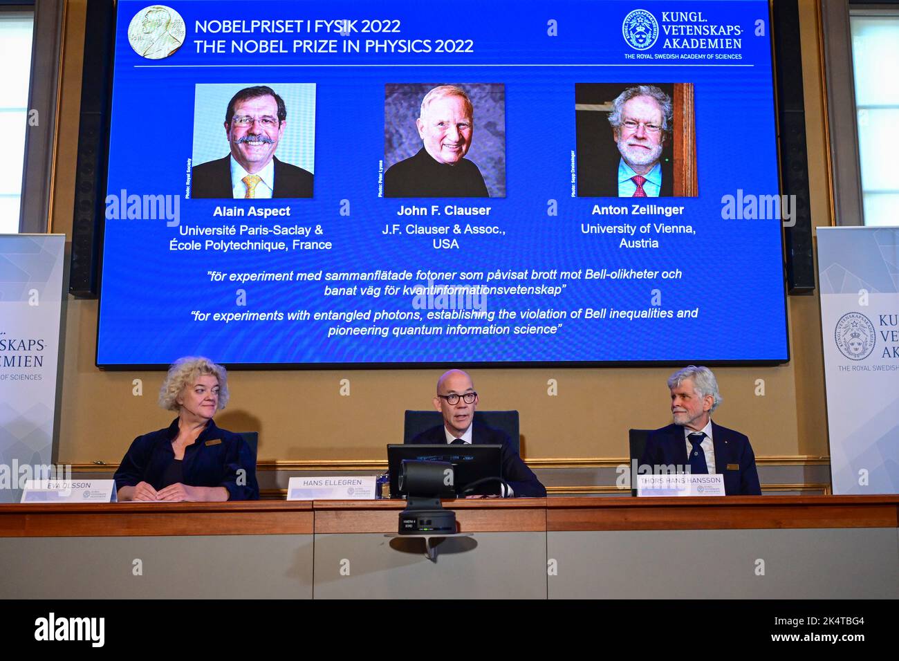 Secretary General of the Royal Swedish Academy of Sciences Hans Ellegren (C), Eva Olsson (L) and Thors Hans Hansson (R), members of the Nobel Committee for Physics announce the winners of the 2022 Nobel Prize in Physics (L-R on the screen)  Alain Aspect, John F. Clauser and Anton Zeilinger, during a press conference at The Royal Swedish Academy of Sciences in Stockholm, Sweden, on October 4, 2022.Photo: Jonas Ekstromer / TT / code 10030 Stock Photo