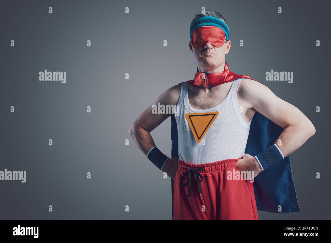 Funny confident superhero posing with arms akimbo, he is wearing a sleep mask over his eyes Stock Photo