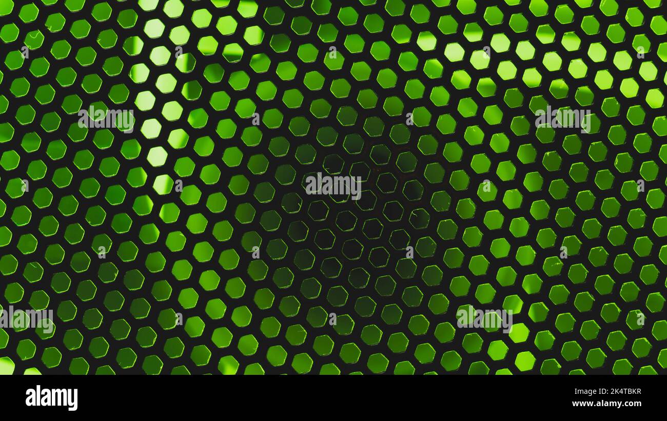 Green light shines through the ventilation grid holes of computer air cooling system. abstract background Stock Photo