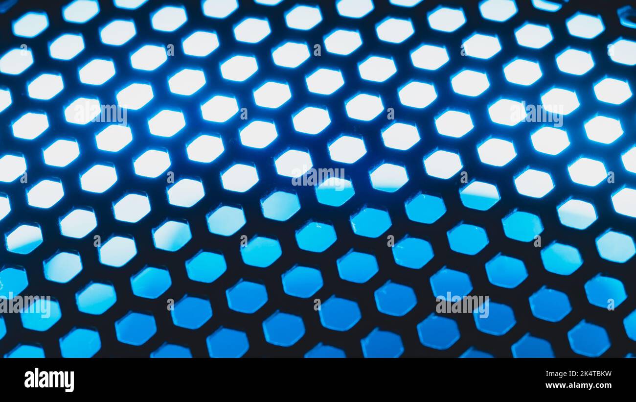 Blue light shines through the ventilation grid holes of computer air cooling system. abstract background Stock Photo