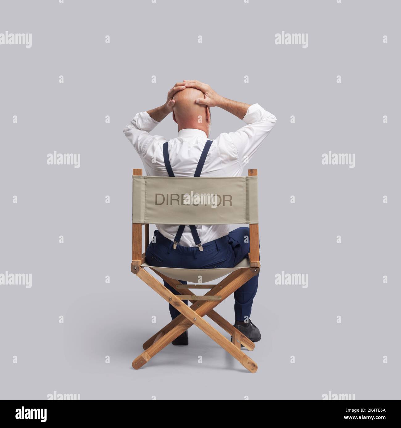 Desperate stressed film director with head in hands, he is sitting on the director's chair, back view Stock Photo