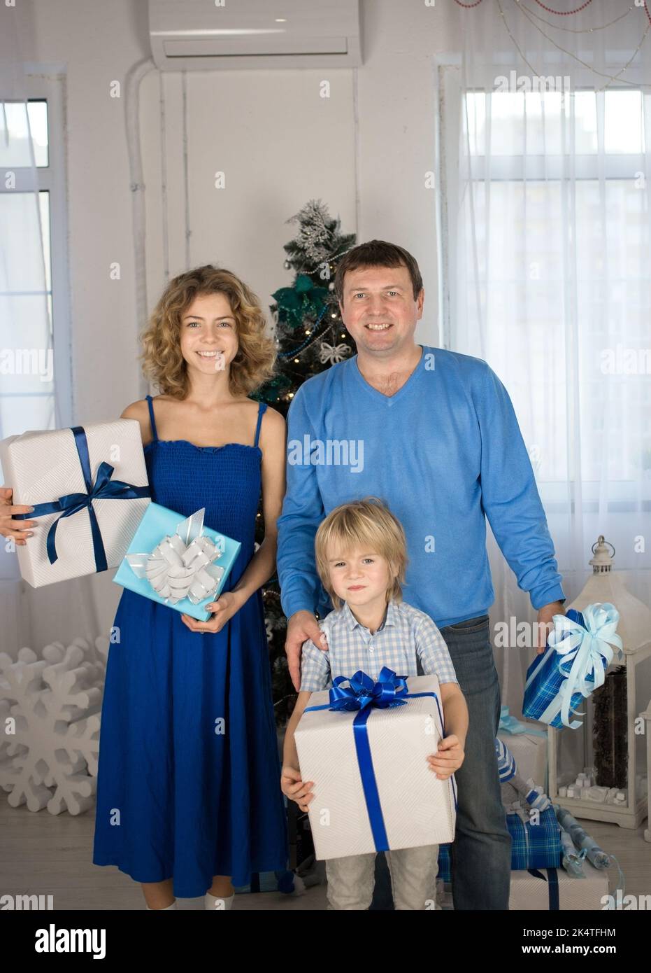 happy family, dad, adult daughter, son 5 years old with gift boxes in hands on Christmas Eve. Bright positive emotions on faces, smile. Blue - white c Stock Photo