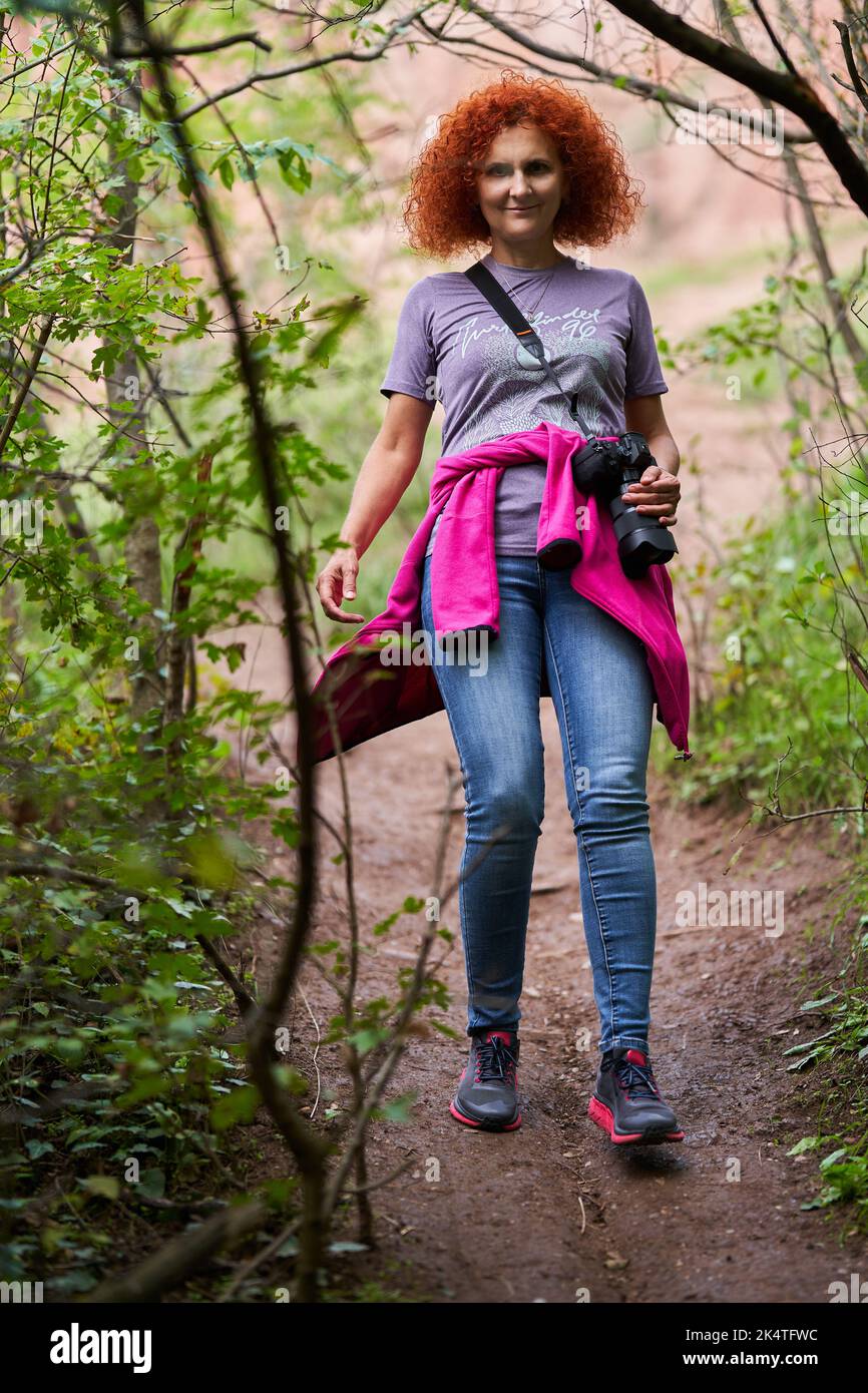 Photographer redhead curly hair woman hiking in the forest with her ...