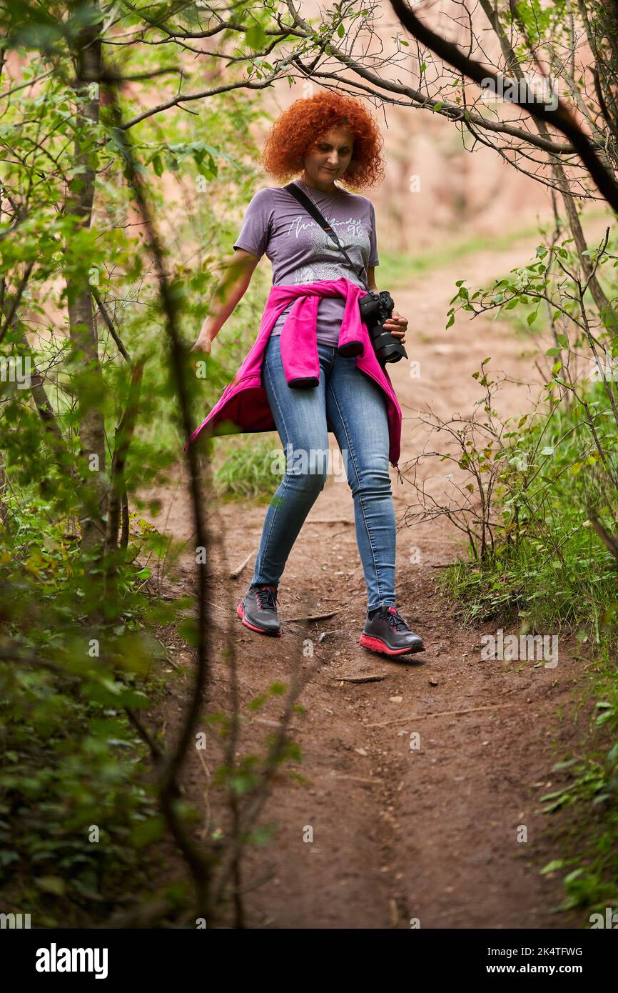 Photographer redhead curly hair woman hiking in the forest with her ...