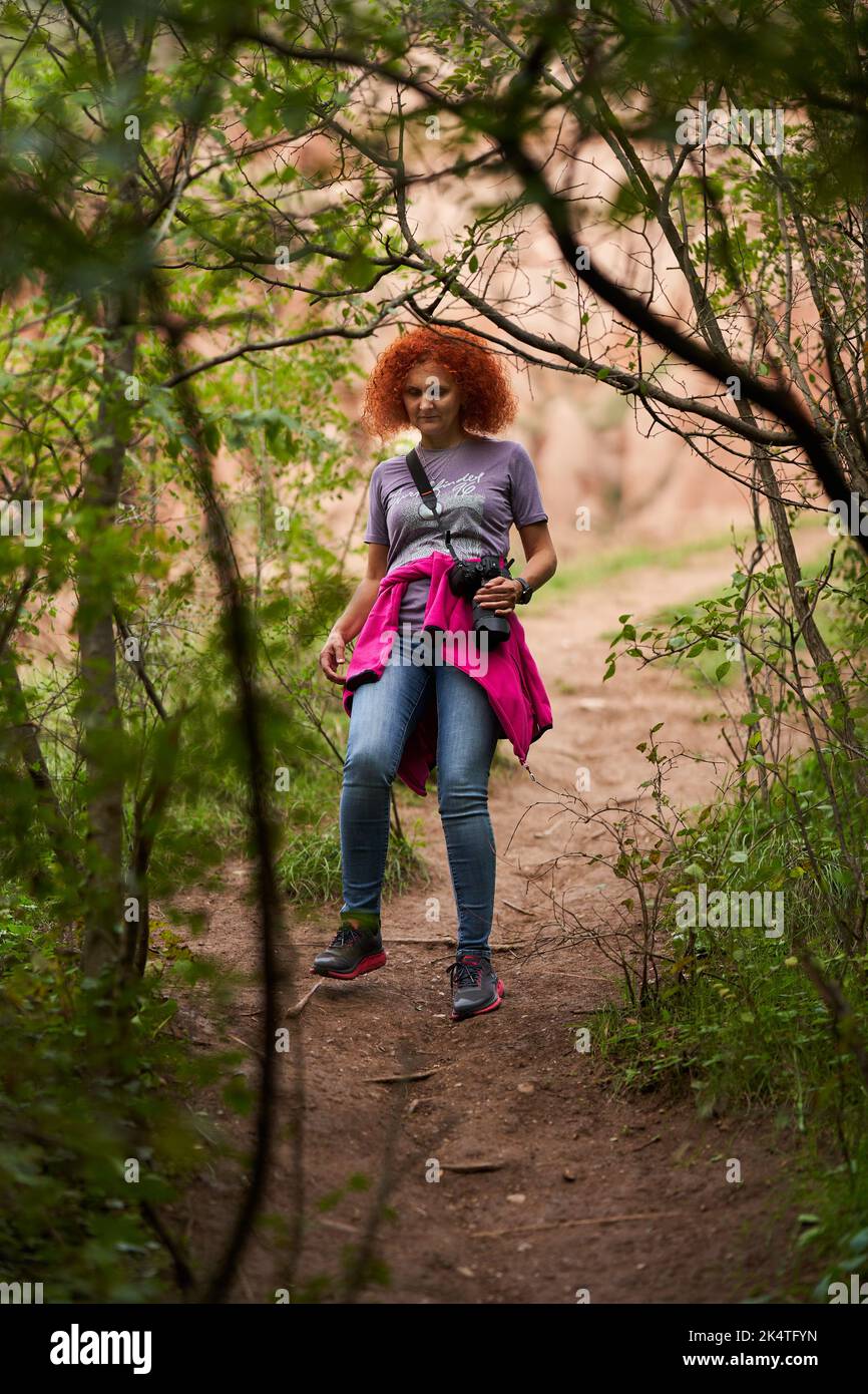 Photographer redhead curly hair woman hiking in the forest with her ...