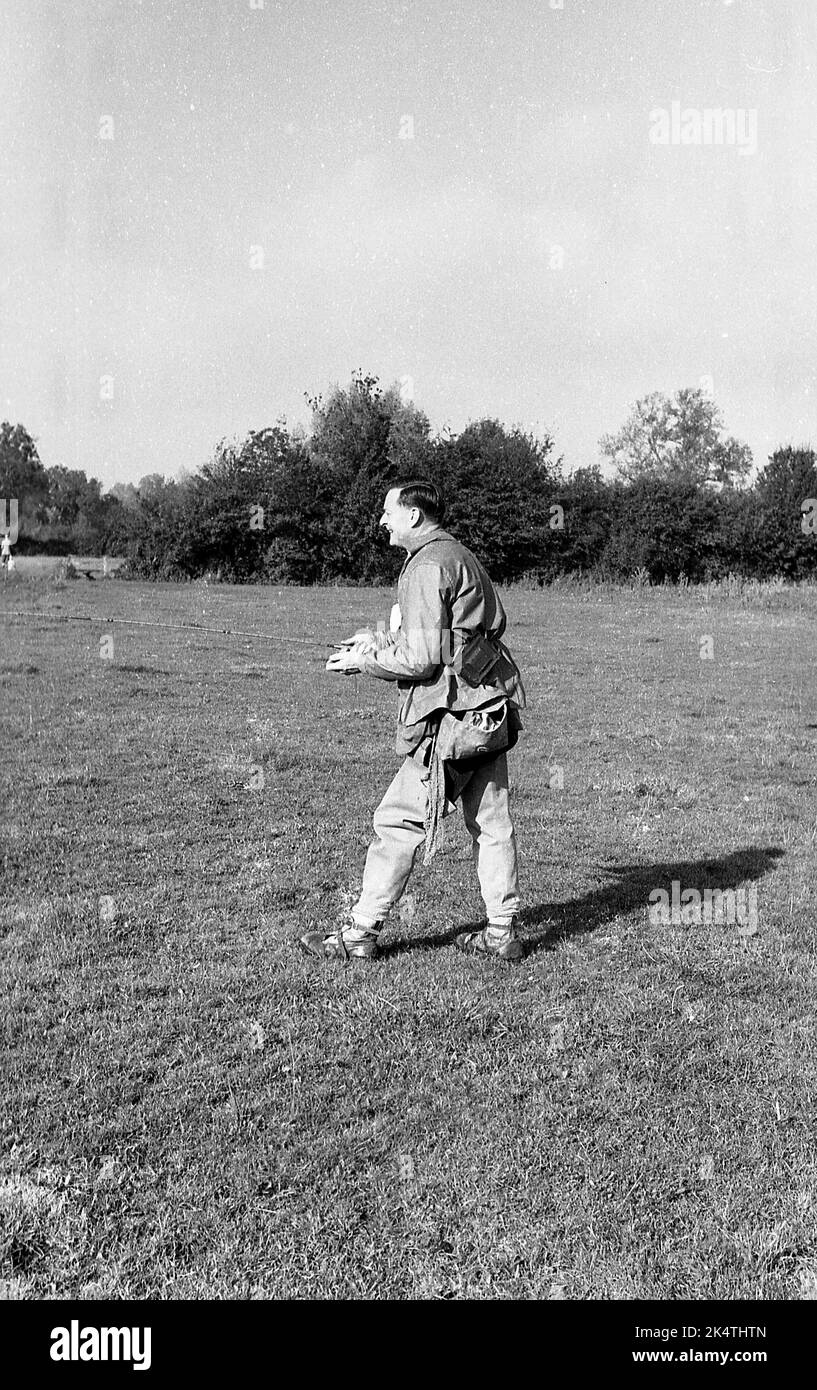 1960s, historical, a coarse fisherman in fishing gear of the, jacket, leg waders and canvas shoulder bag, standing on some flat ground on the riverbank, fishing several yards from the river, Twekesbury, Glos, England, UK. Stock Photo